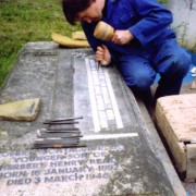 stonemason hand cutting a raised lead inscription